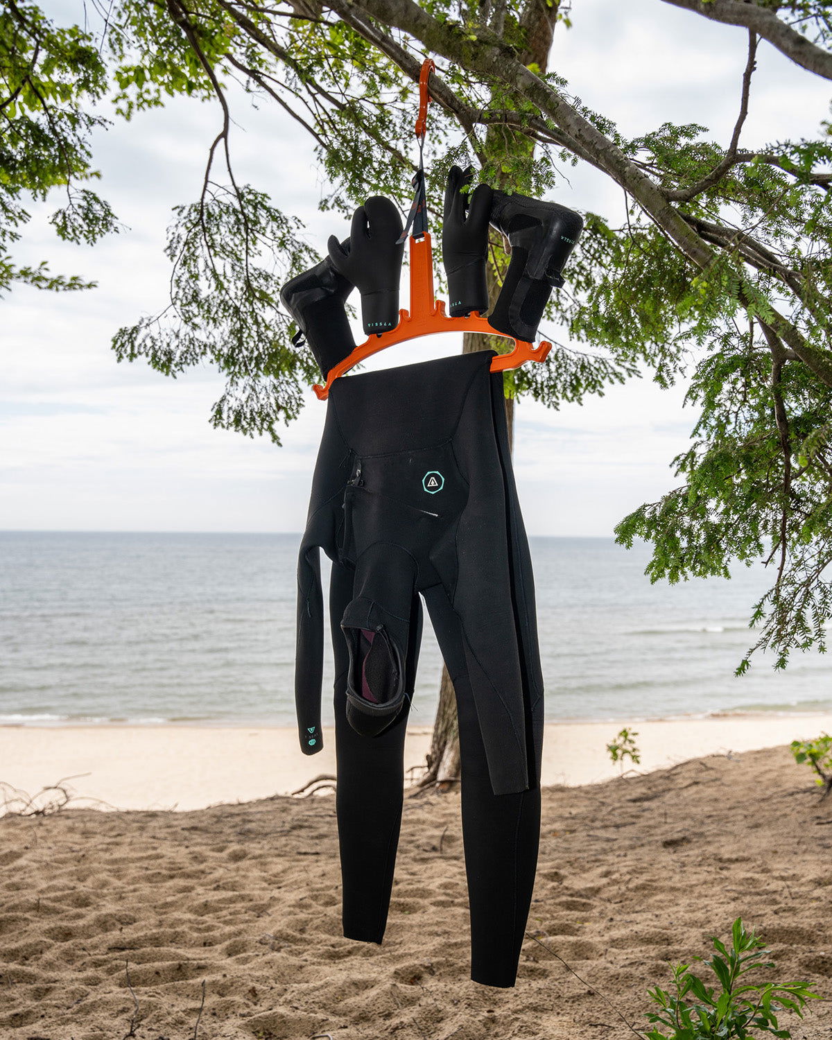 C-Monsta orange wetsuit hanger in use – full wetsuit with gloves hanging from tree on sandy beach